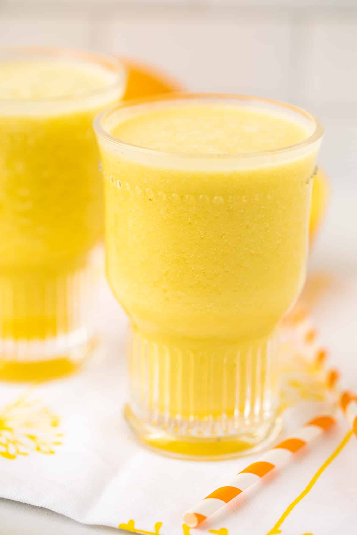 pineapple orange coconut smoothie with an orange striped straw.