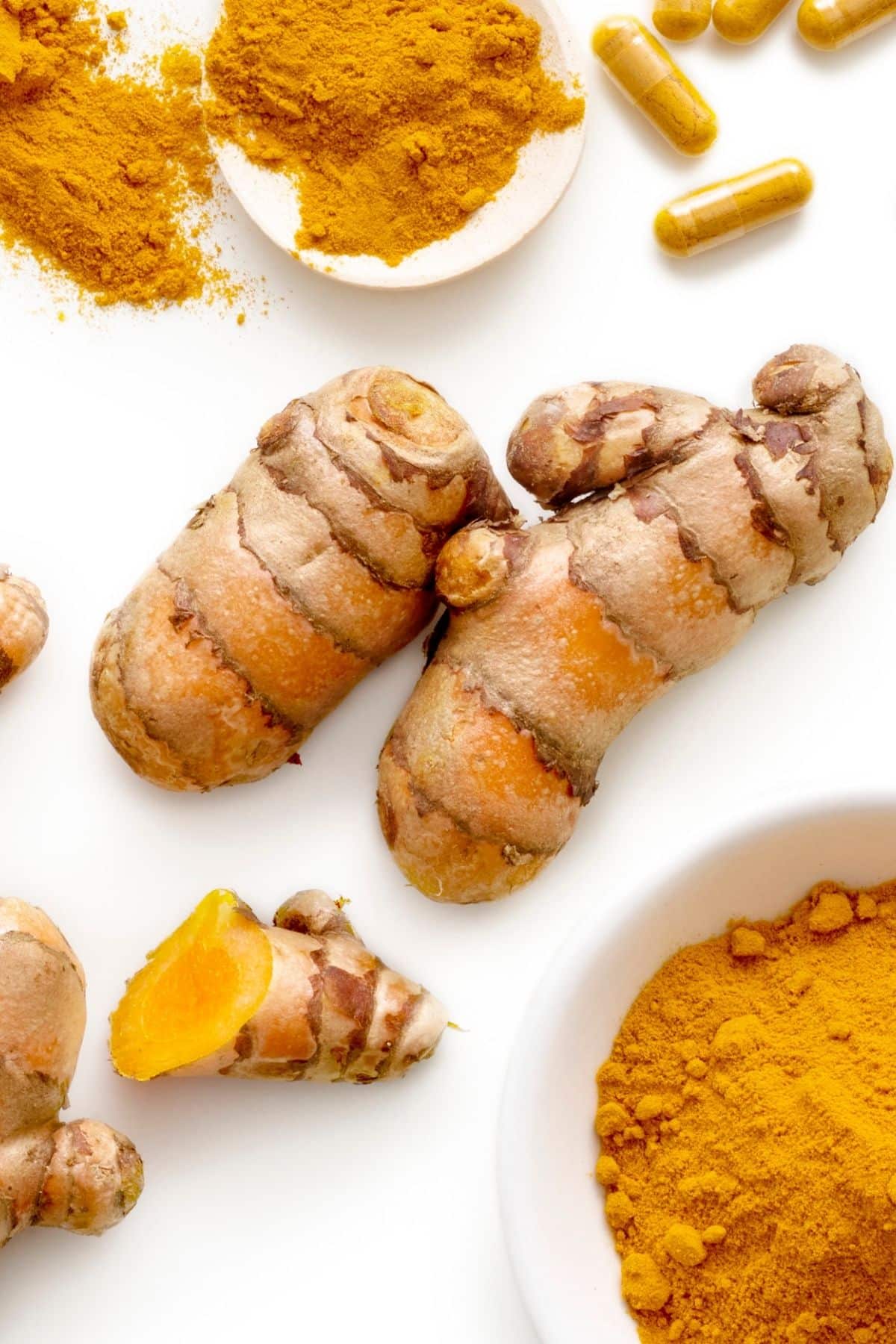 turmeric root on a table with ground turmeric in a bowl.