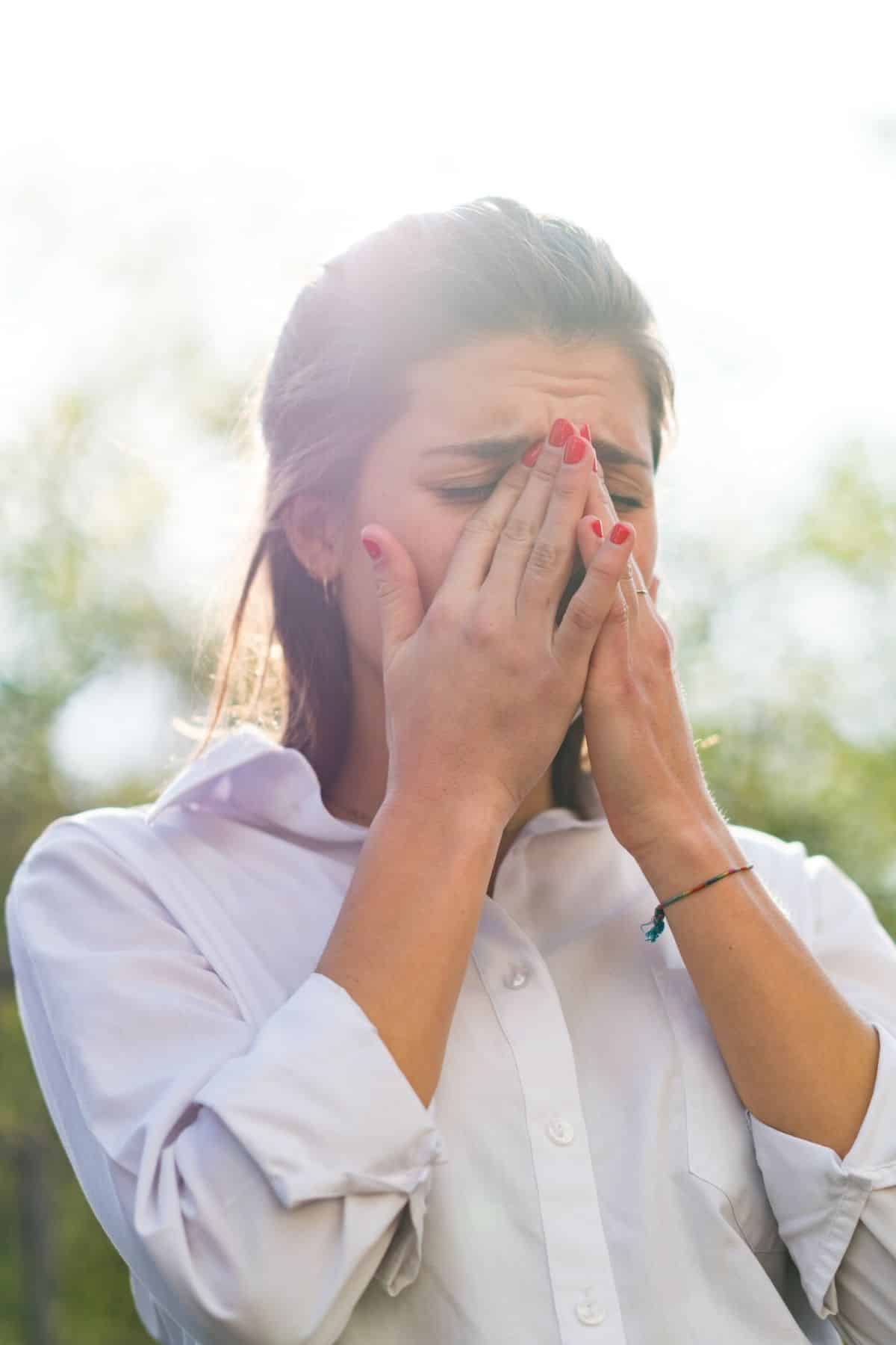 woman outside holding her nose.