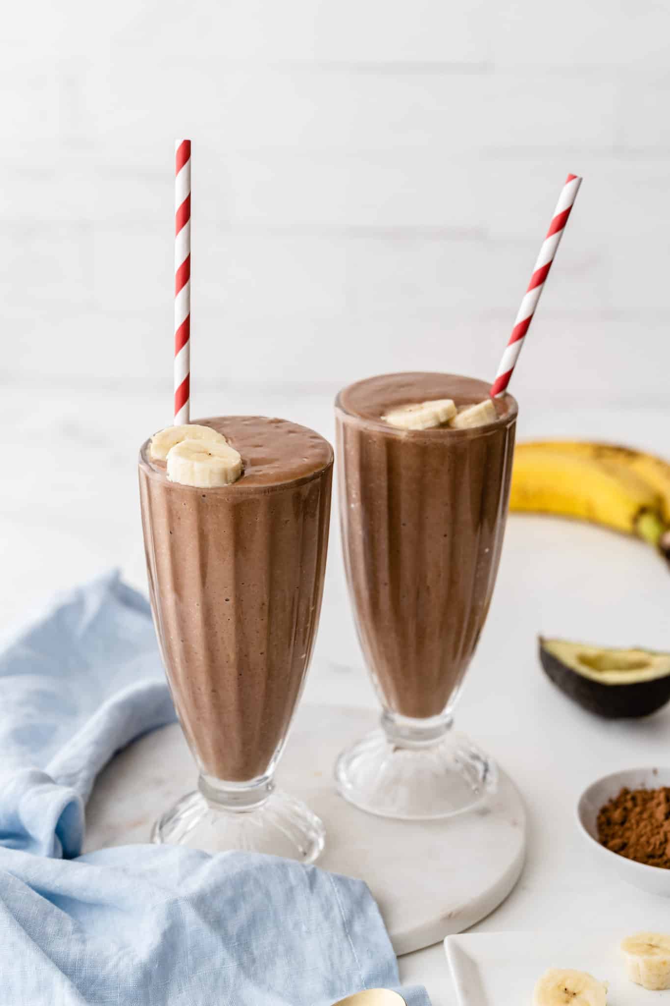 Chocolate avocado smoothies served in two milkshake glasses with straws.