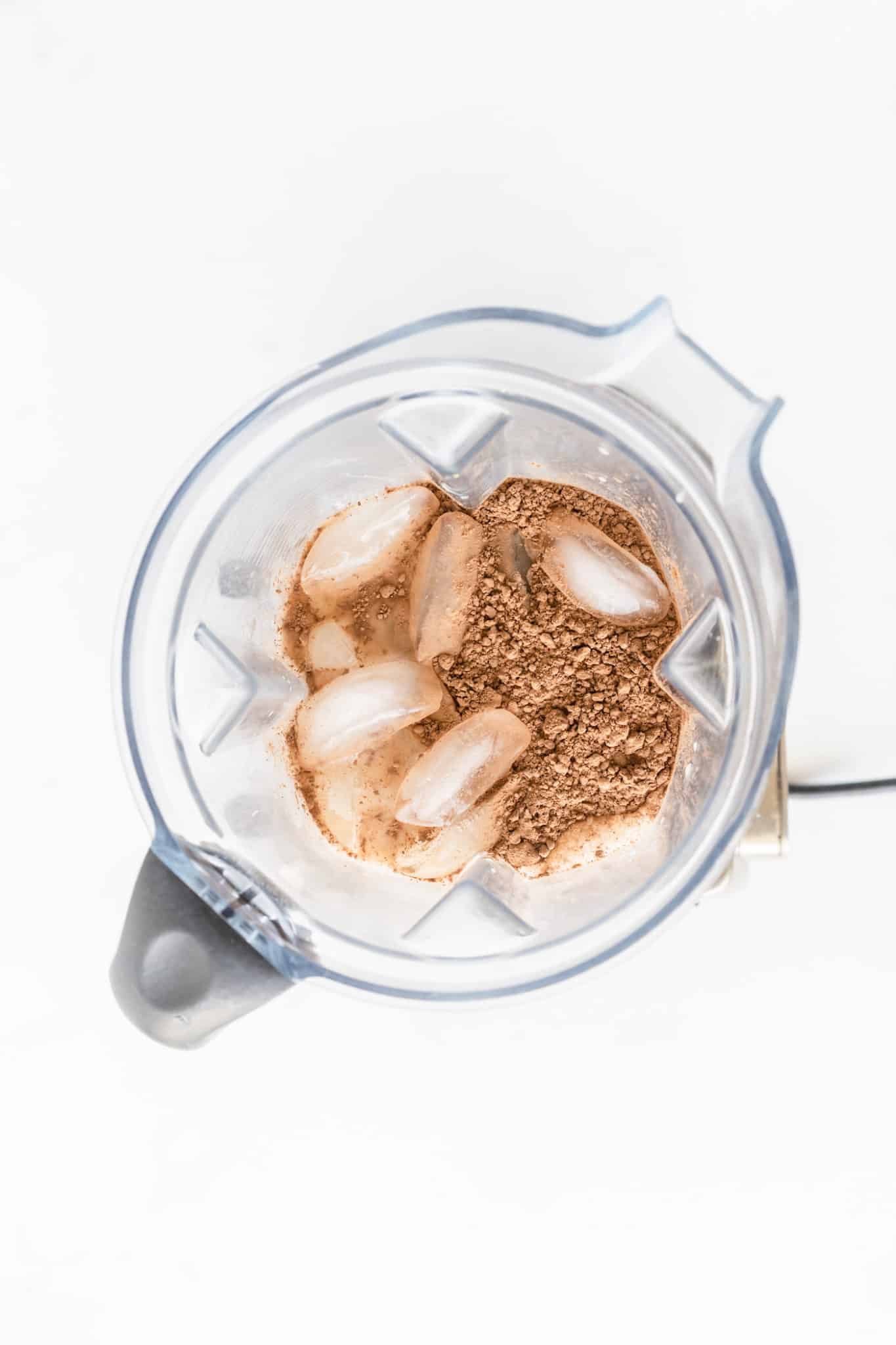 Cocoa powder and ice in a blender to make avocado smoothie.