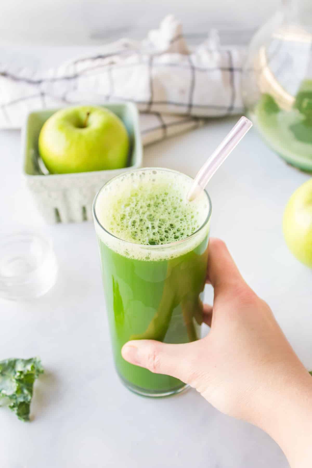 hand reaching for glass of green juice with a straw.