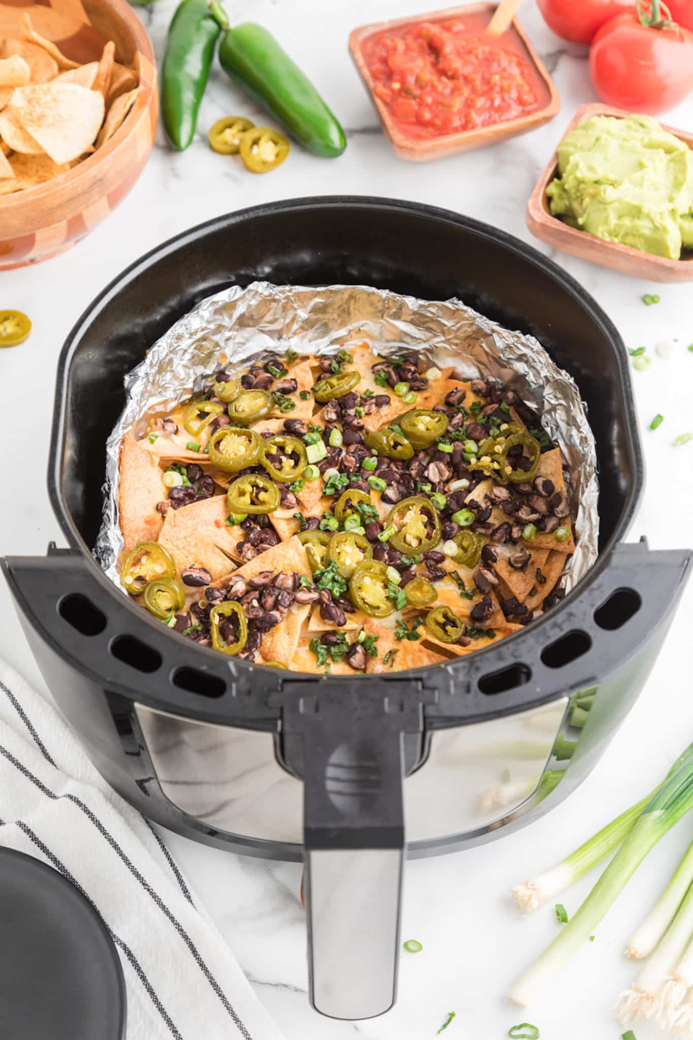 cooked nachos inside of air fryer basket with a foil liner.