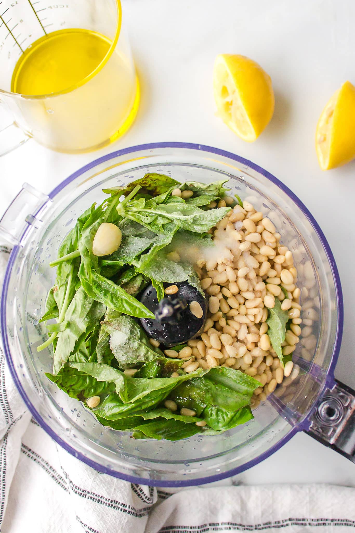 Basil and pine nuts in the bowl of a food processor to make pesto.