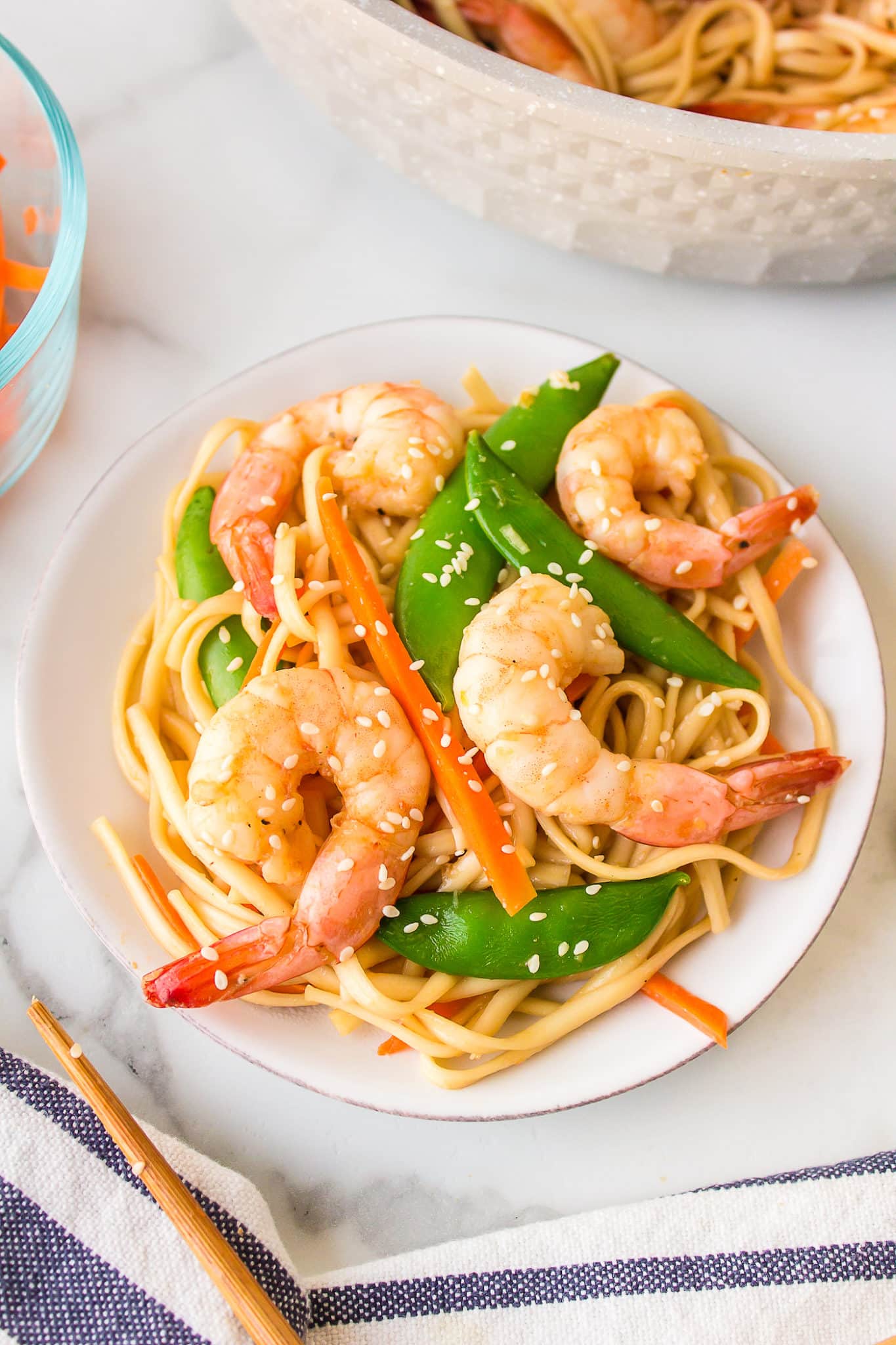 Shrimp udon with peas and peppers on a small white plate.