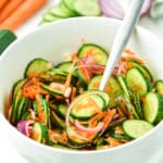 A forkful of cucumber carrot salad over a small white bowl full.