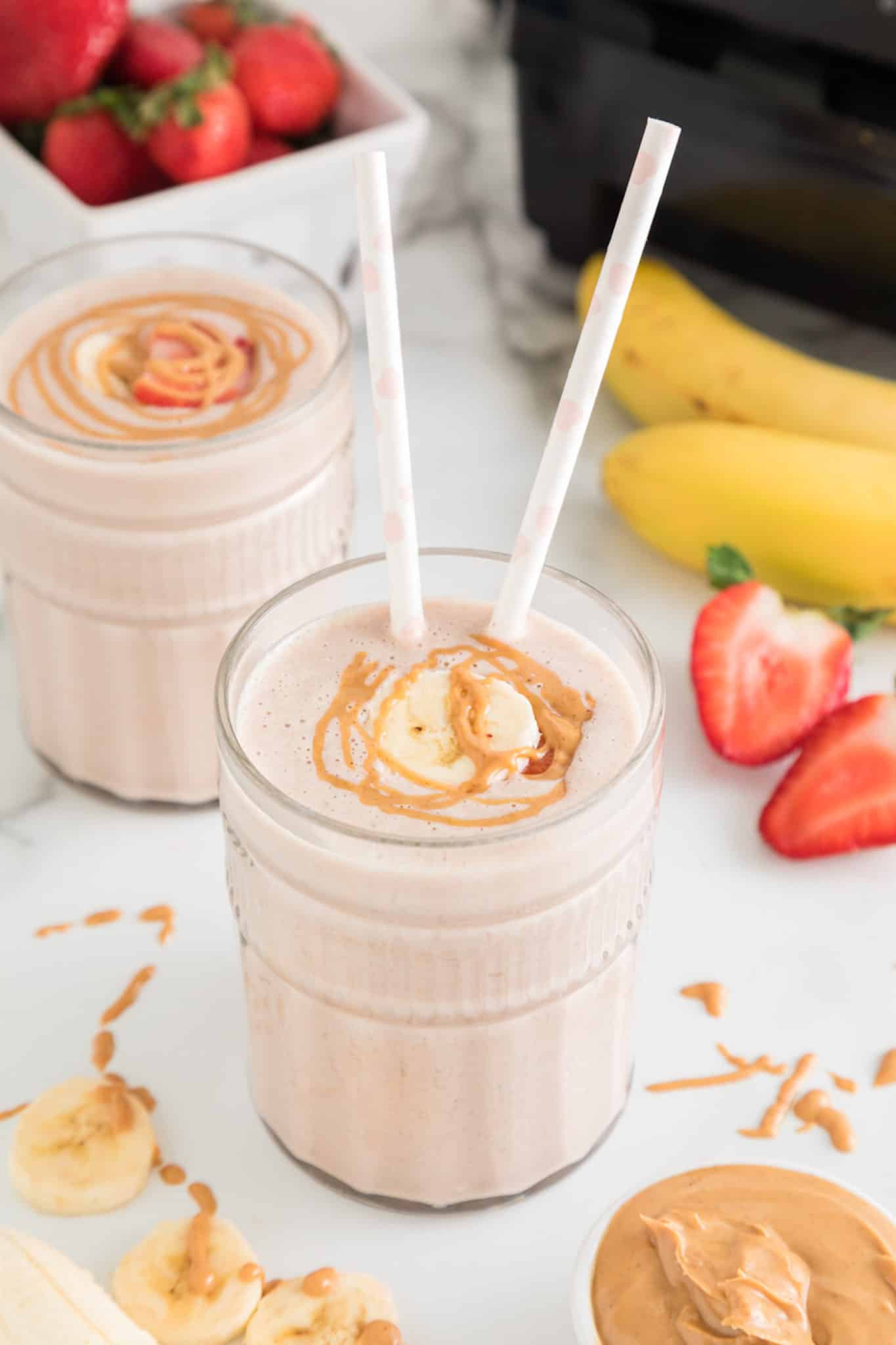 Strawberry Banana smoothie in a glass with two straws and peanut butter drizzled on top.