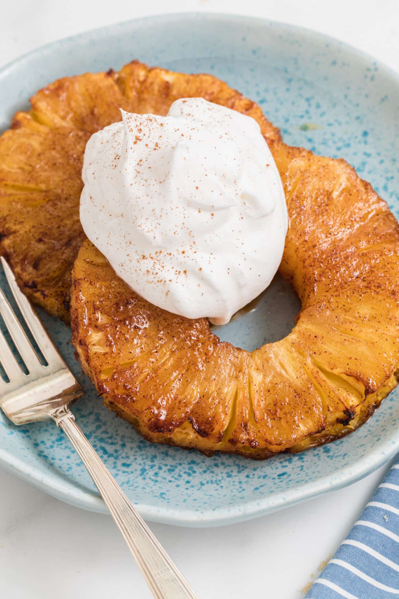 air fryer grill pineapple on plate with whipped cream and fork.