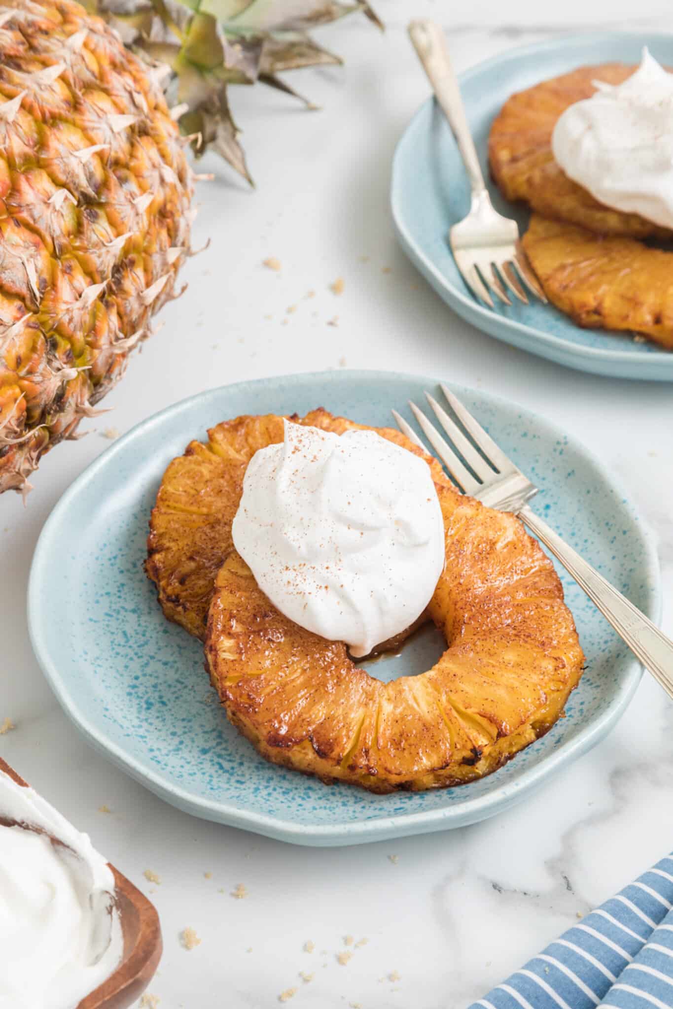 Two air fried pineapple rings topped with whipped cream on a small blue plate.