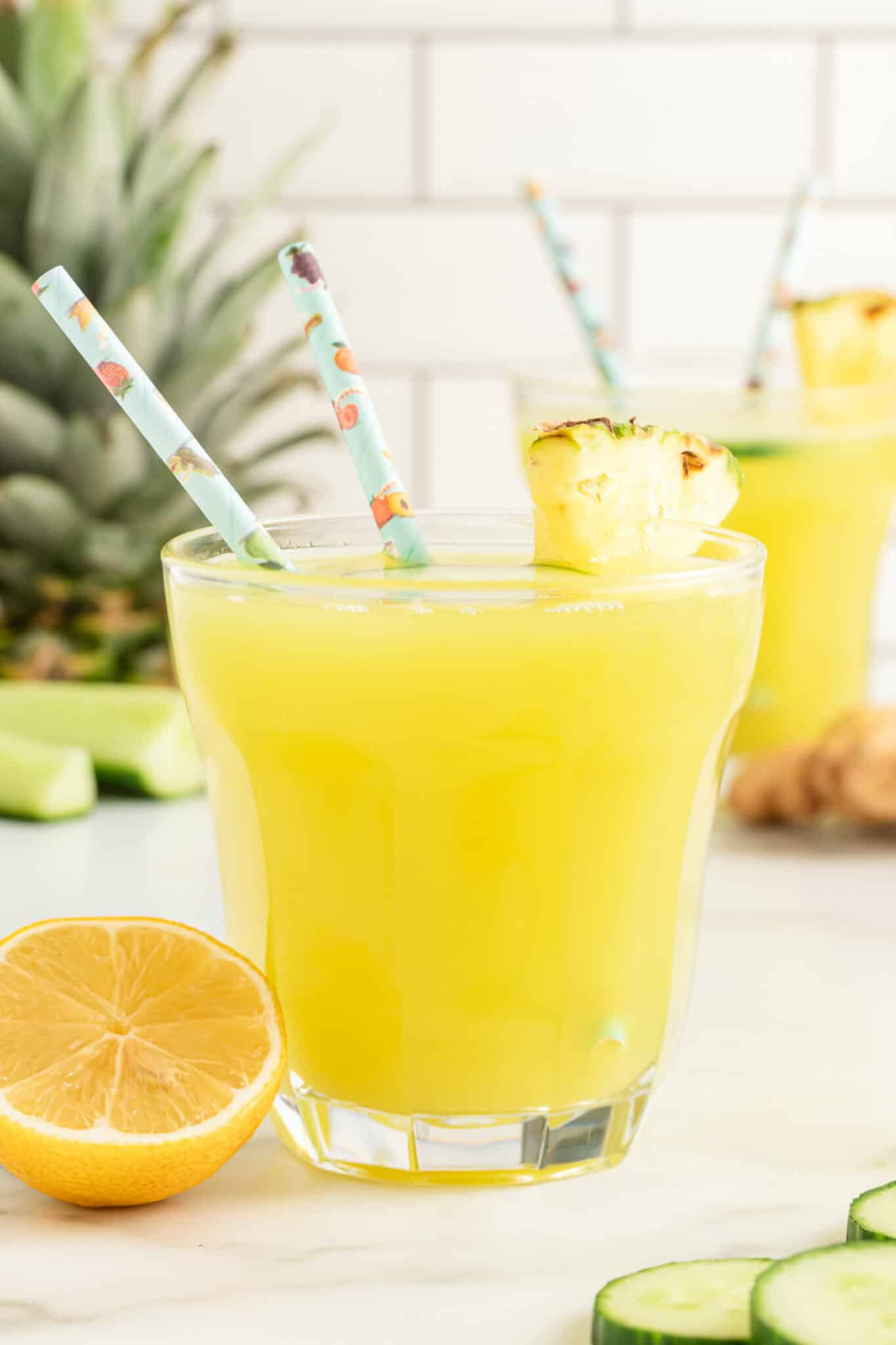 Closeup of a glass of pineapple cucumber juice with two straws.