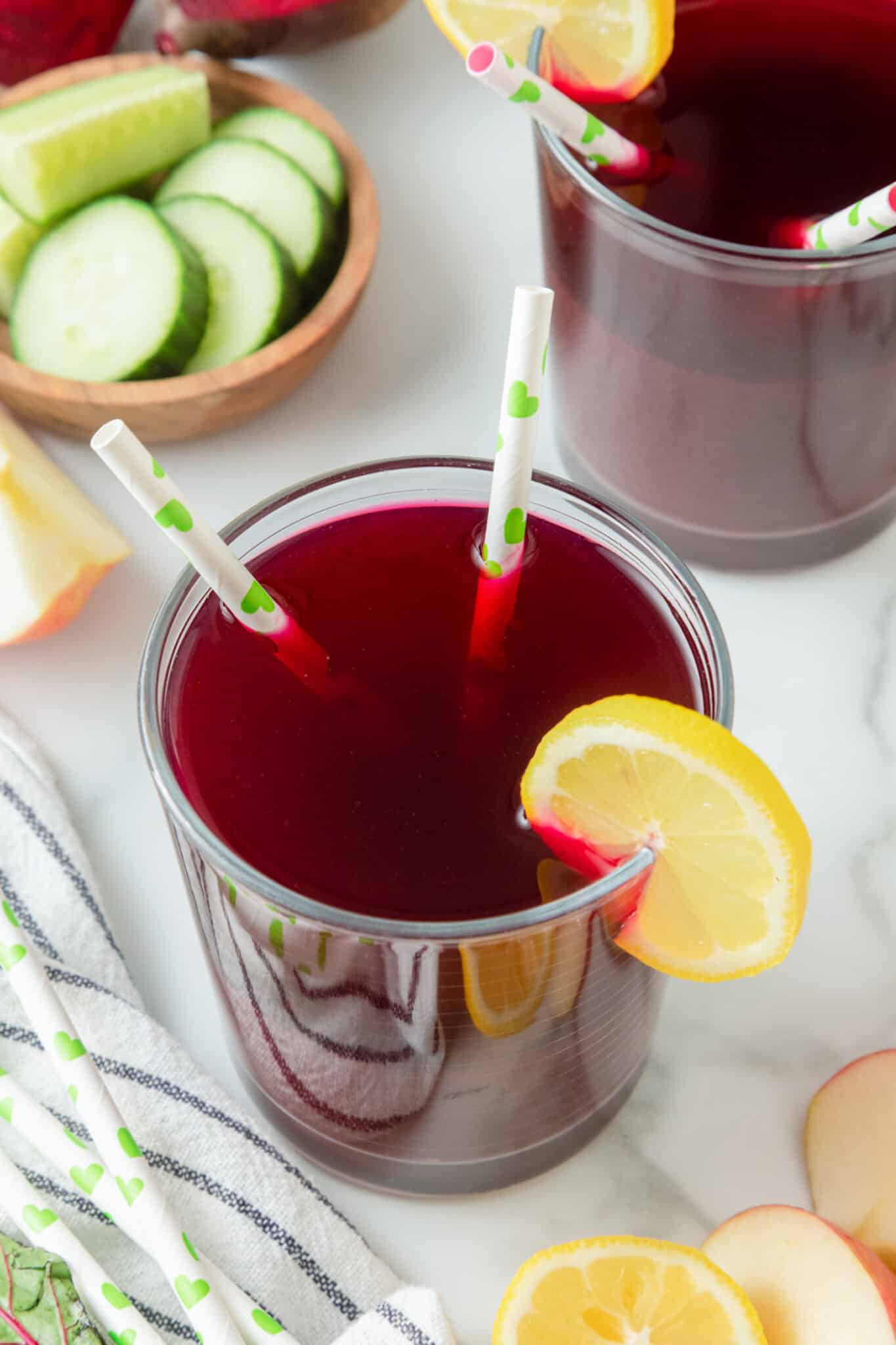 A glass of red juice with two straws and a lemon slice.