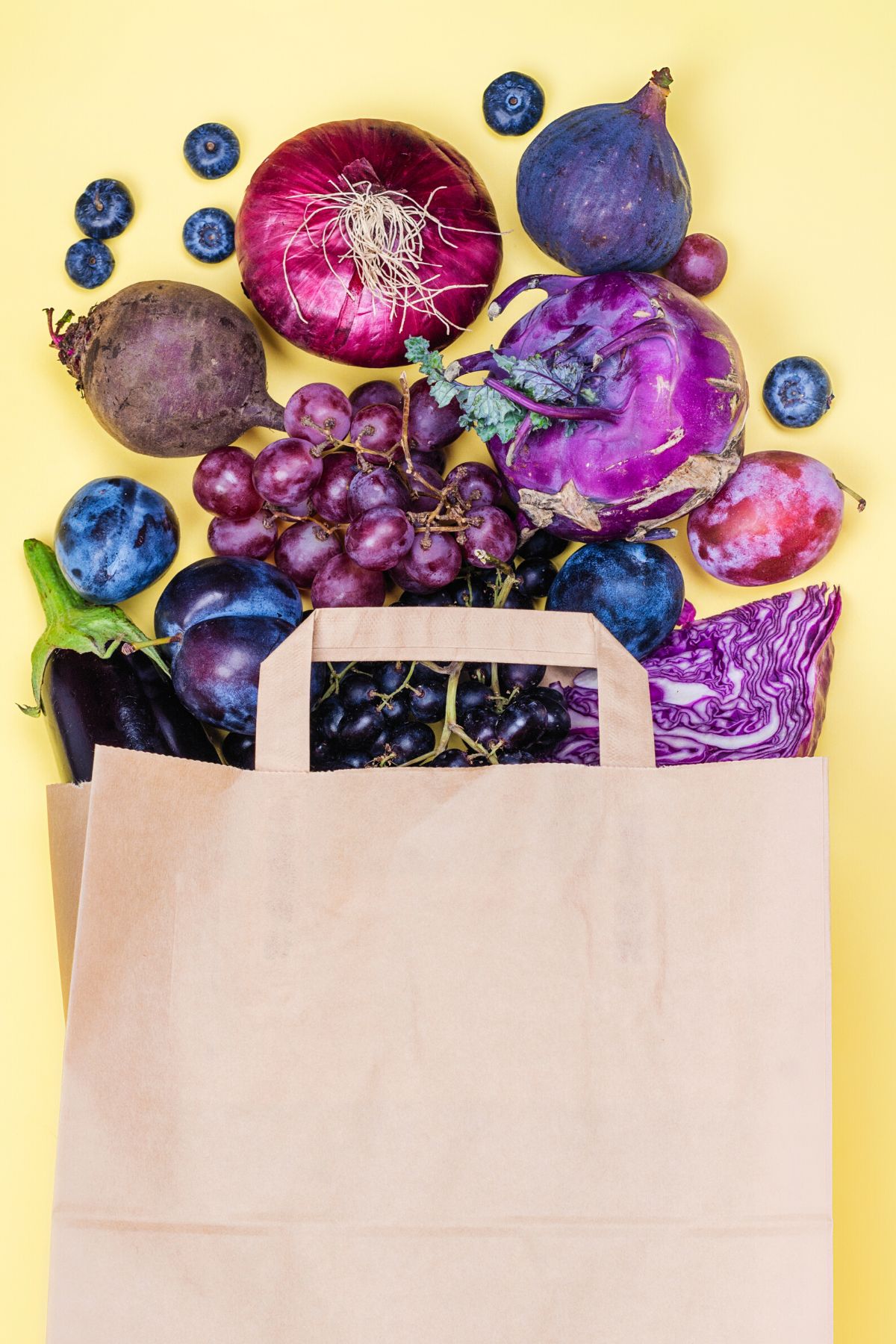 Many blue and purple fruits and veggies spilling out of a paper bag.