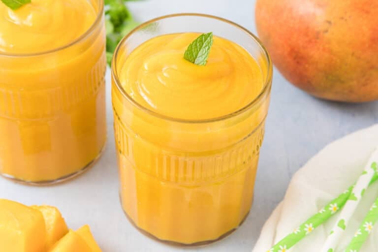 A glass of mango juice topped with a mint leaf.