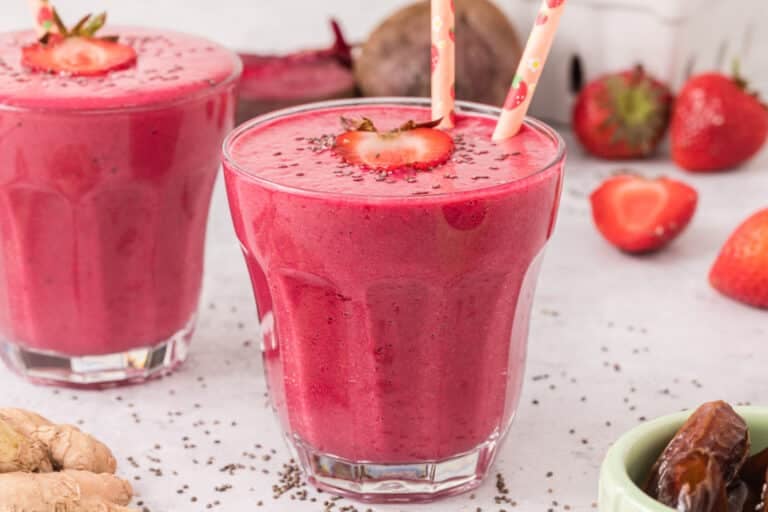 Two pink straws in a glass of strawberry smoothie topped with strawberries and chia.