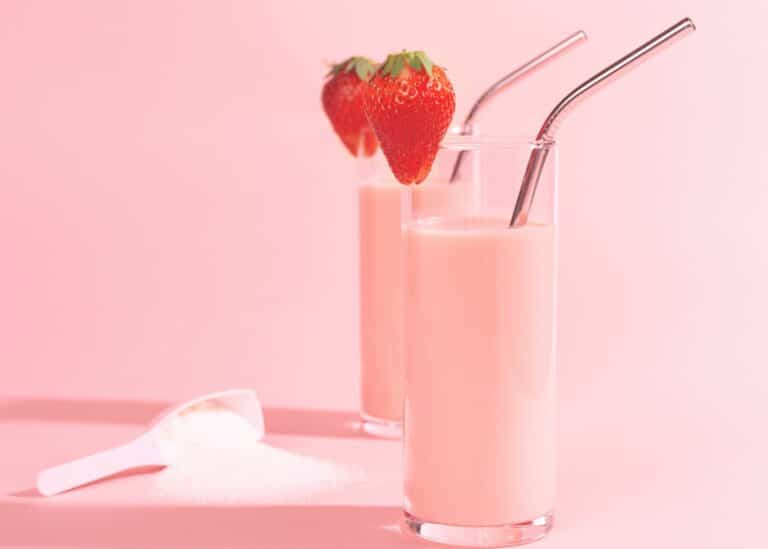 Two tall glasses of strawberry protein smoothies with metal straws.