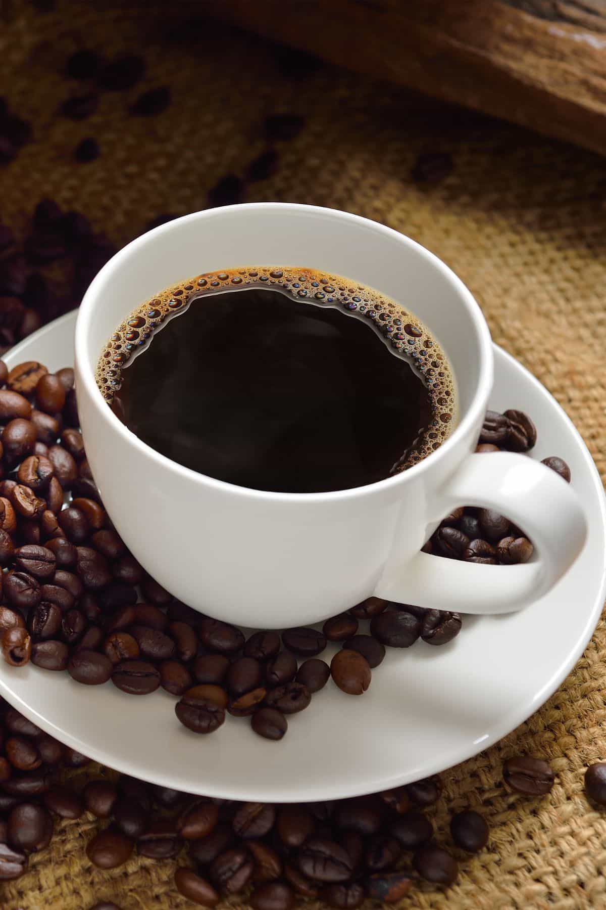 a mug of coffee surrounded by coffee beans.