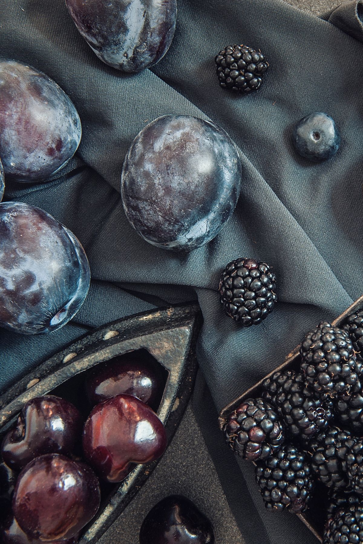 a variety of blue fruits on a navy tablecloth.