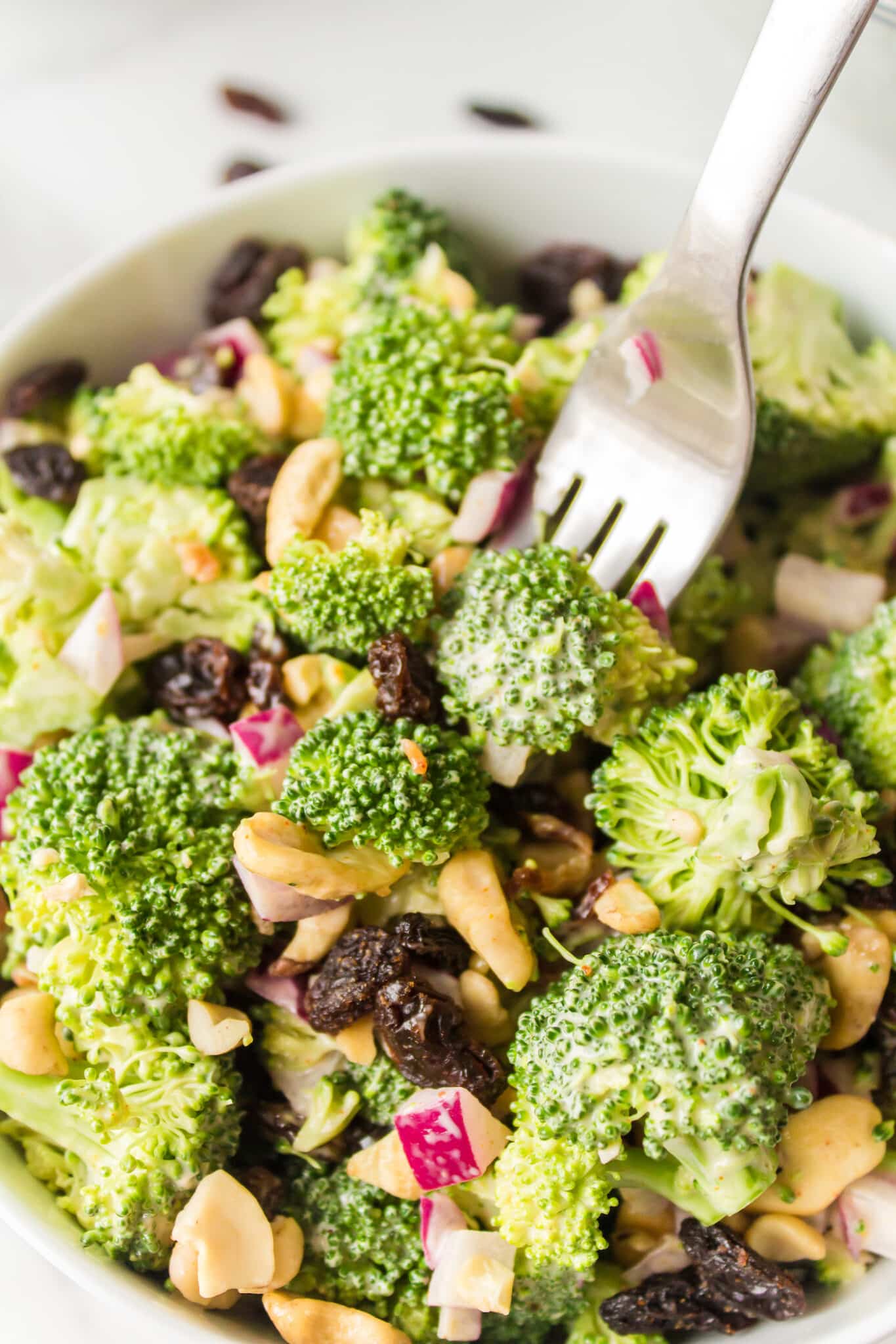 Broccoli crunch salad with raisins and cashews in a white bowl.