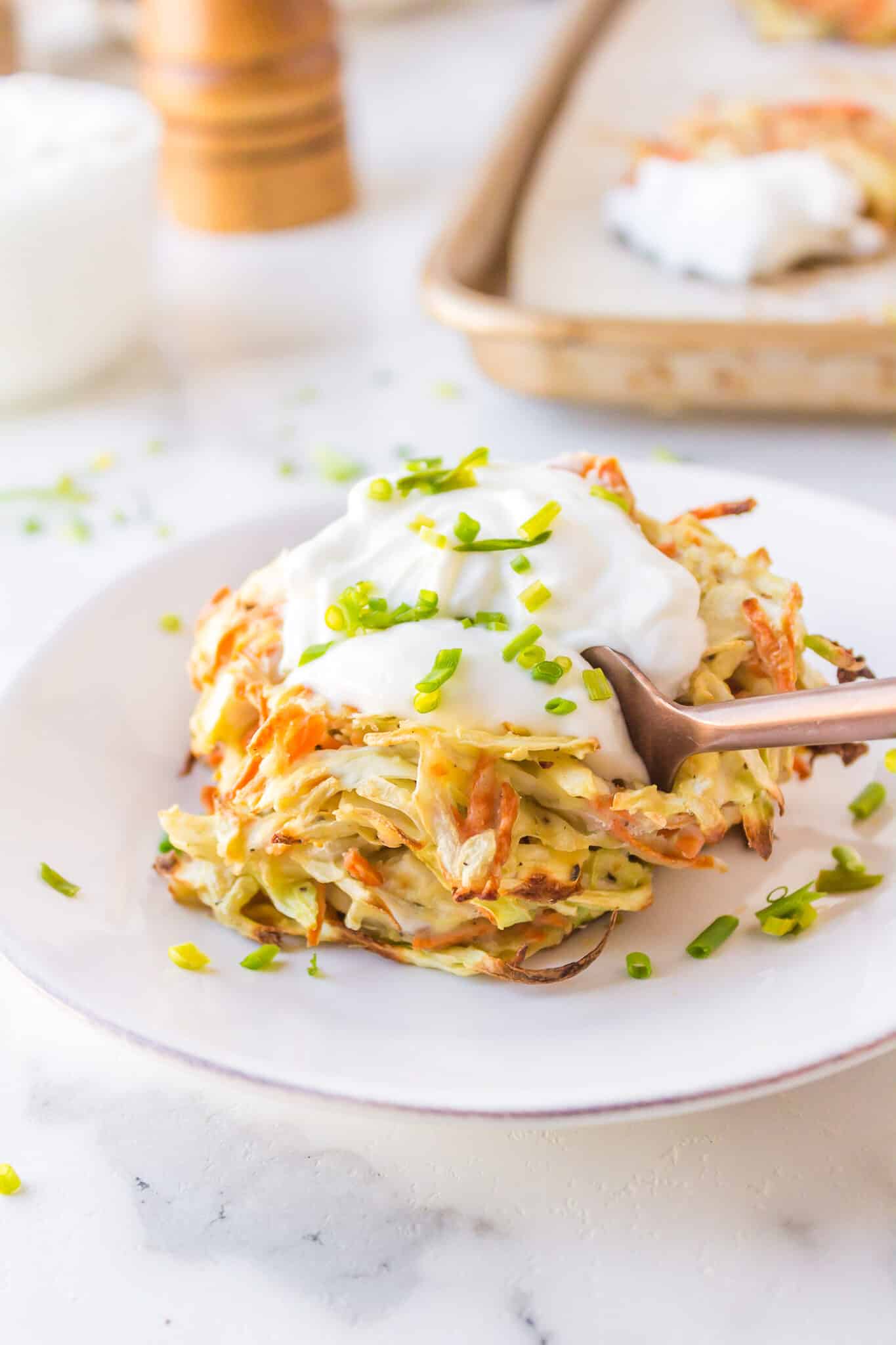 cabbage fritters served on plate with sour cream and fork.