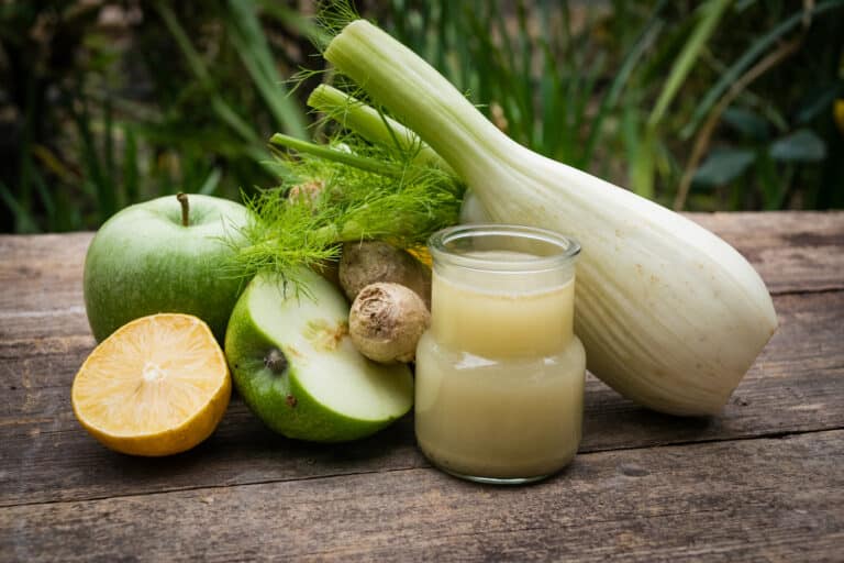 A glass of fennel juice next to fennel, apple, and ginger.