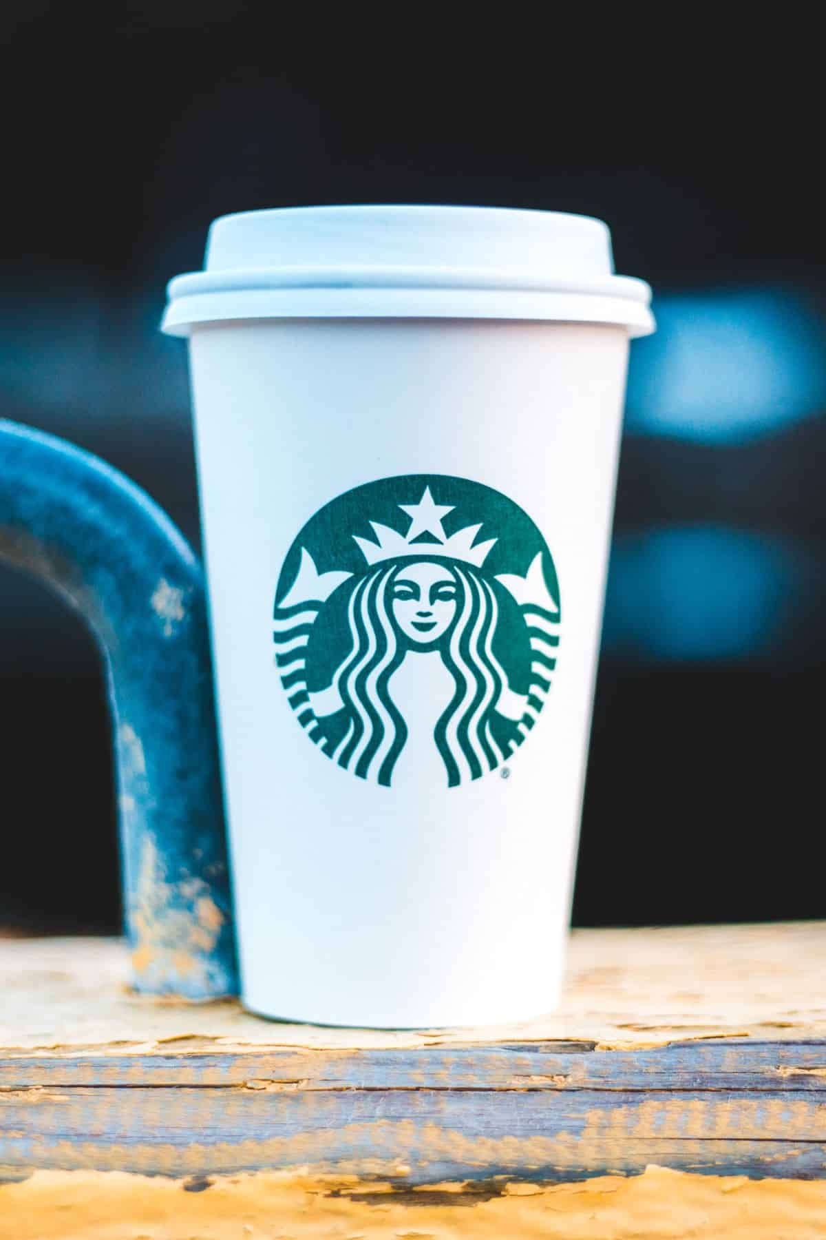 a Starbucks cup sitting on a wooden bench.