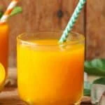 A short glass of mango carrot juice with a striped straw.