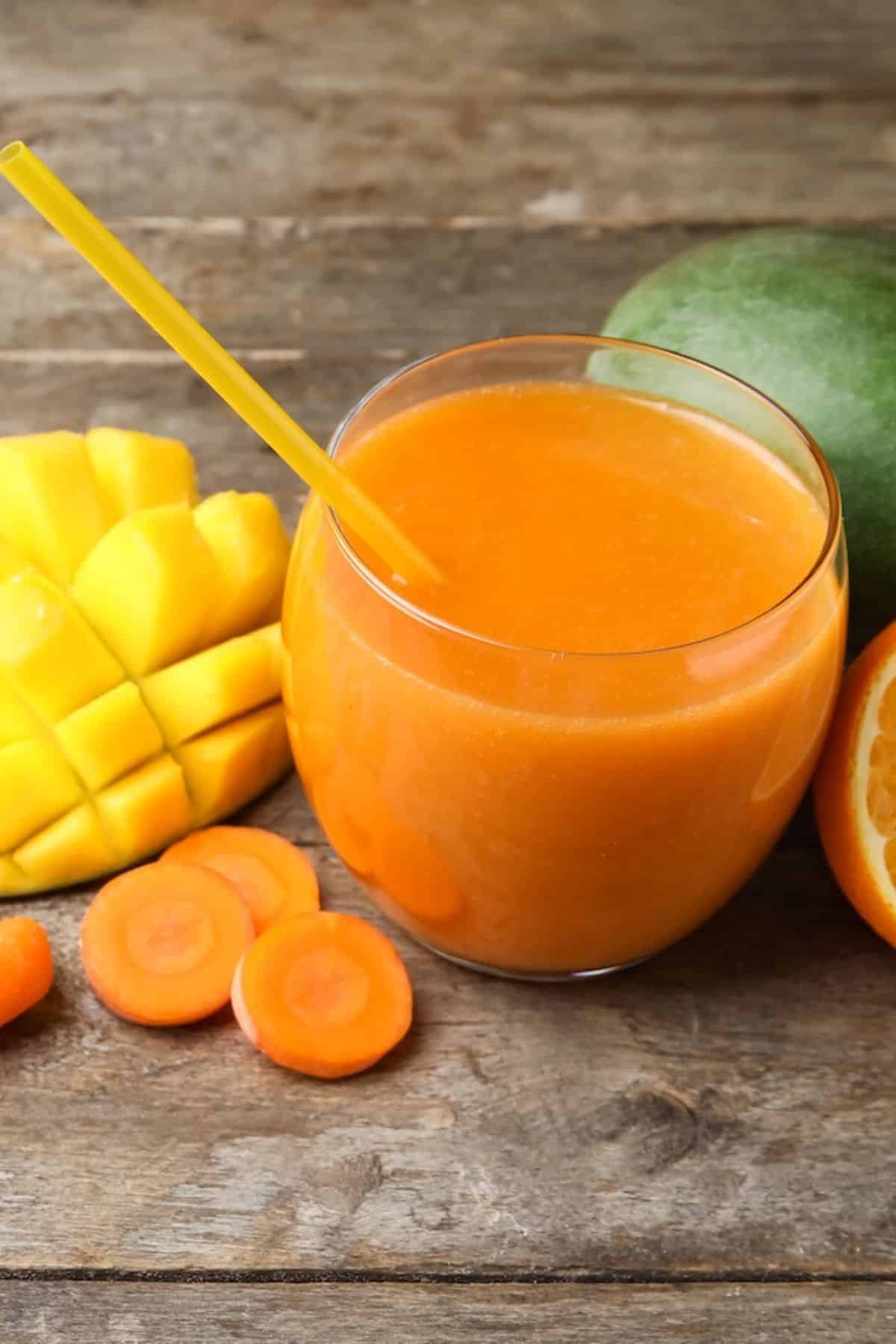 A short glass of carrot mango juice with a yellow straw.