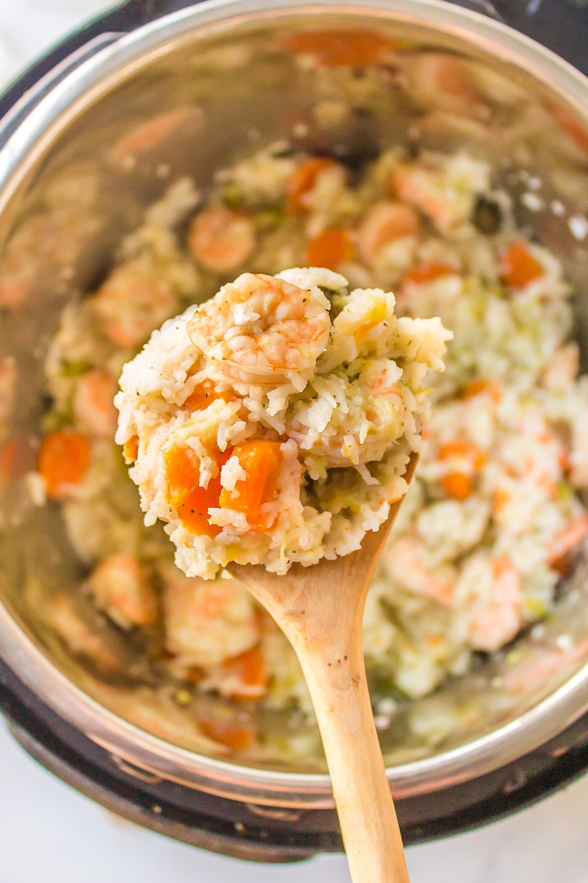 A wooden spoon showing off a scoop of rice and shrimp over an Instant Pot.