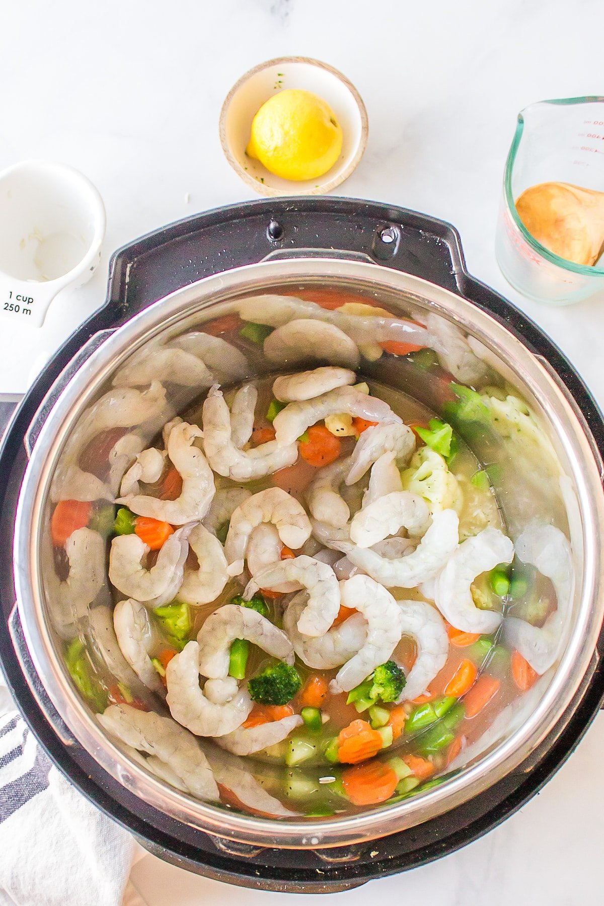 Raw shrimp on top of veggies and broth in an Instant Pot.