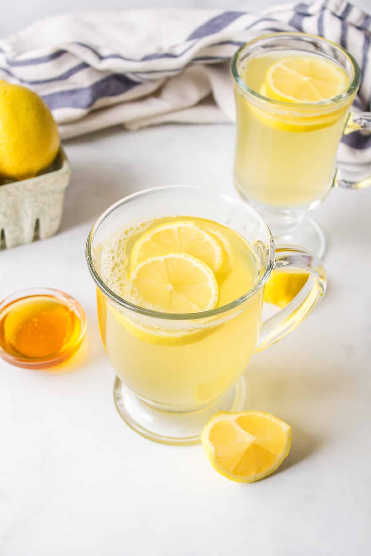 clear mug with honey lemon tea topped with sliced lemon.