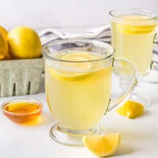 two mugs of honey lemon tea on table.