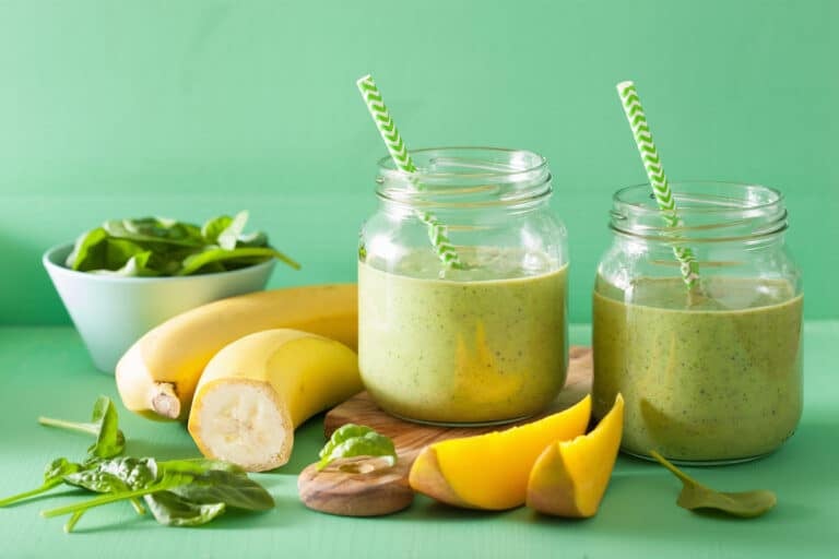 two weight loss green smoothies next to bananas and mango.