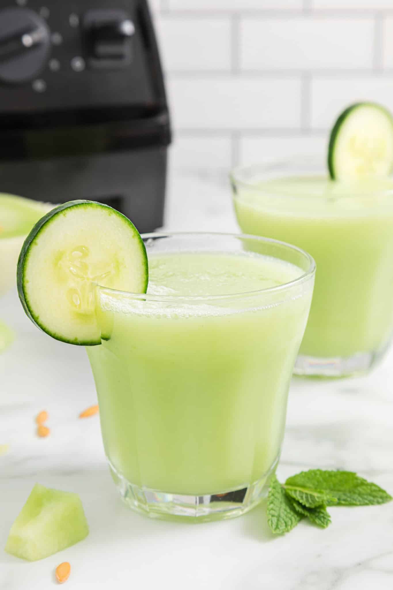 cucumber smoothie served in two glasses on table.