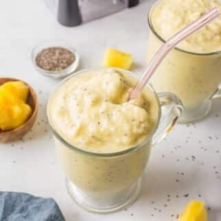 pineapple smoothie in glass with straw and ingredients.