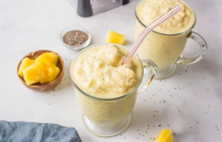 pineapple smoothie in glass with straw and ingredients.