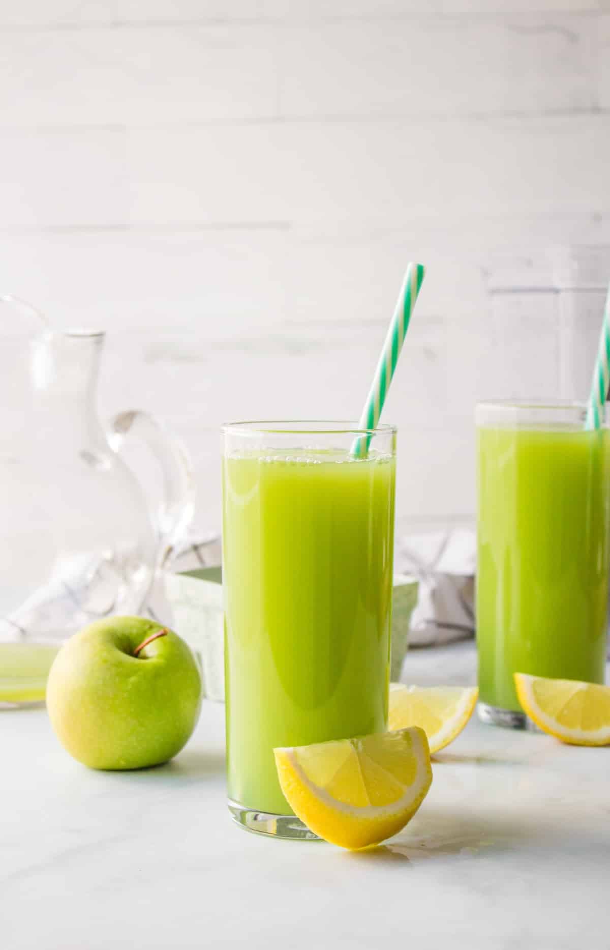 two glasses of cucumber apple juice with straws.